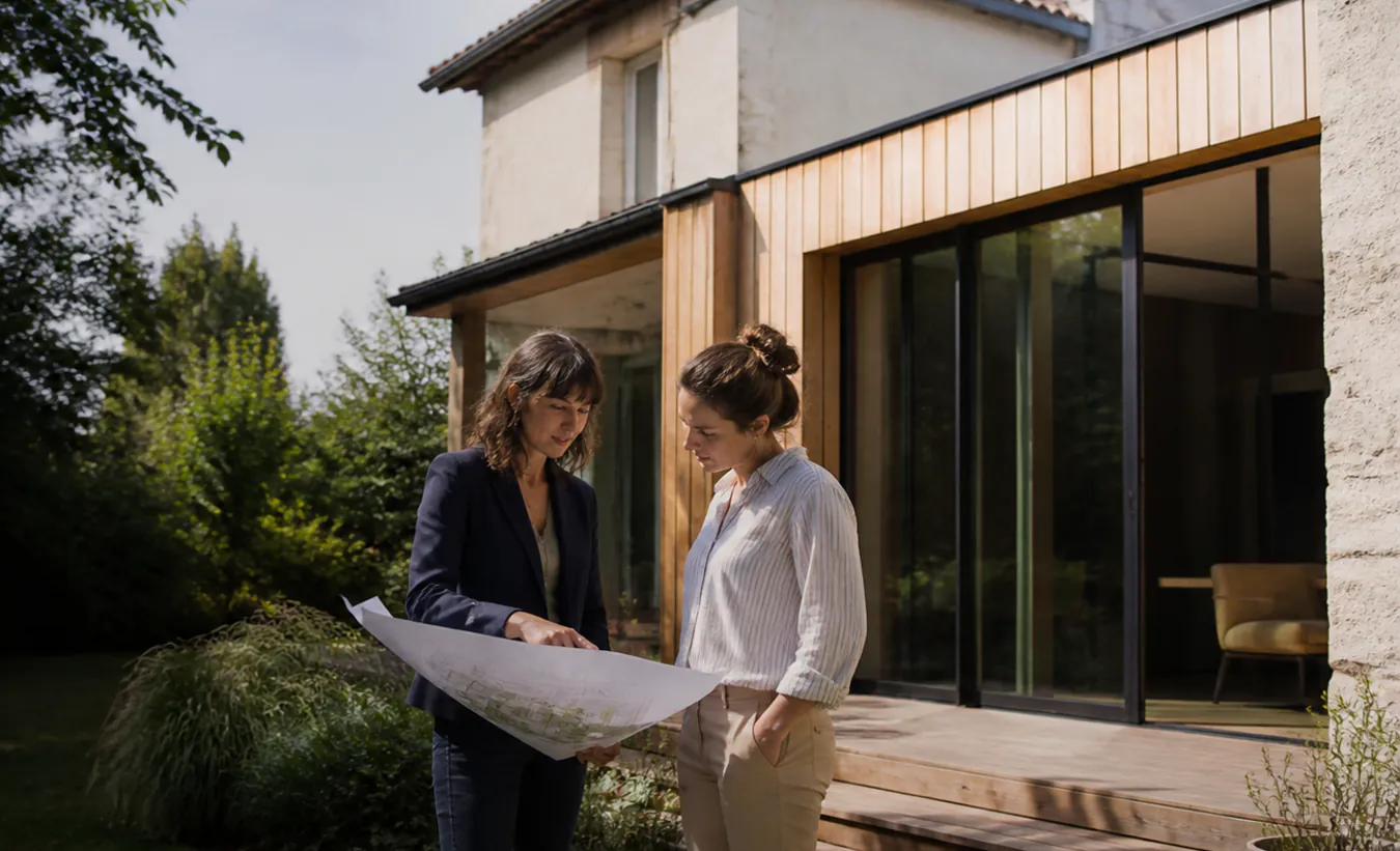 Une architecte et une propriétaire examinent une extension de maison de l'intérieur de la France en pierre et enduit clair