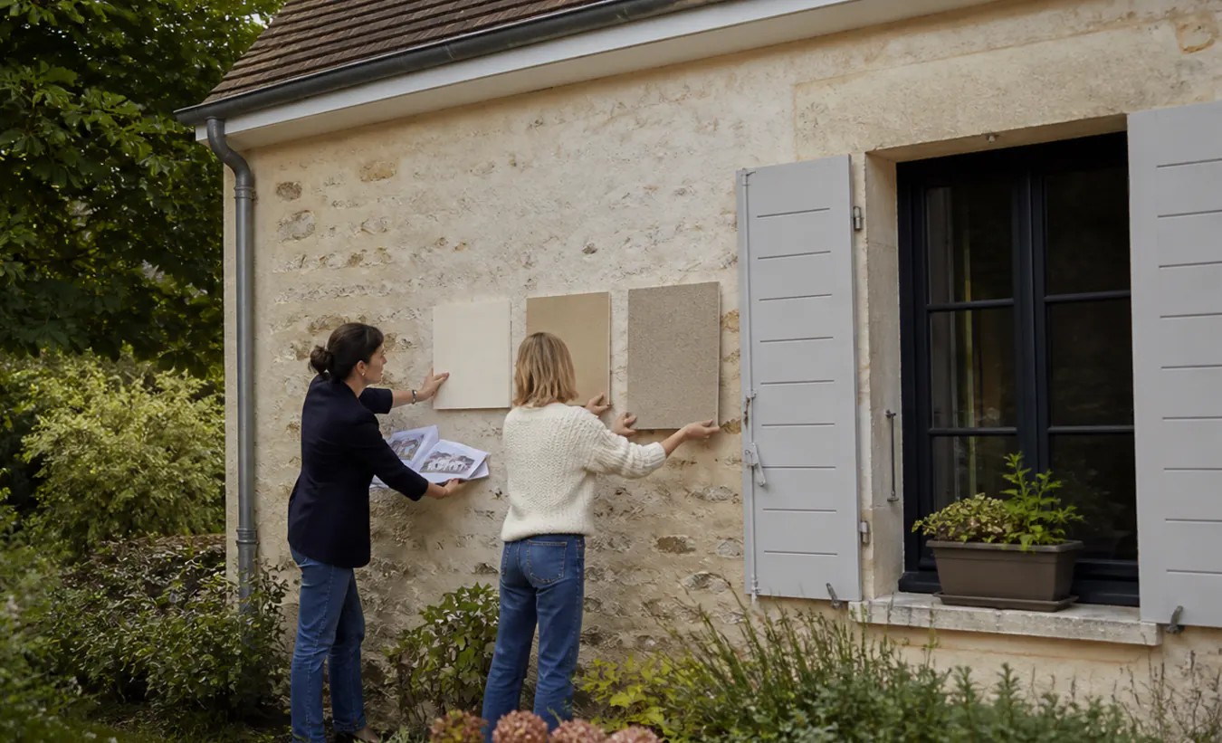 Une architecte et une propriétaire comparent des matériaux de façade devant une maison de l'intérieur de la France en pierre et enduit clair