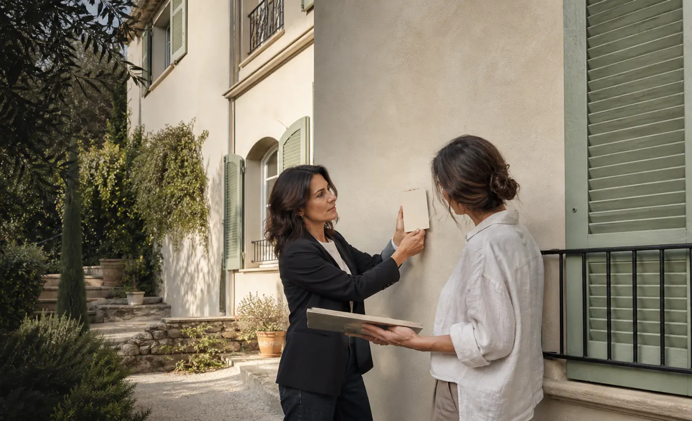 Une architecte présente une teinte de façade à une propriétaire devant une villa aux volets peints