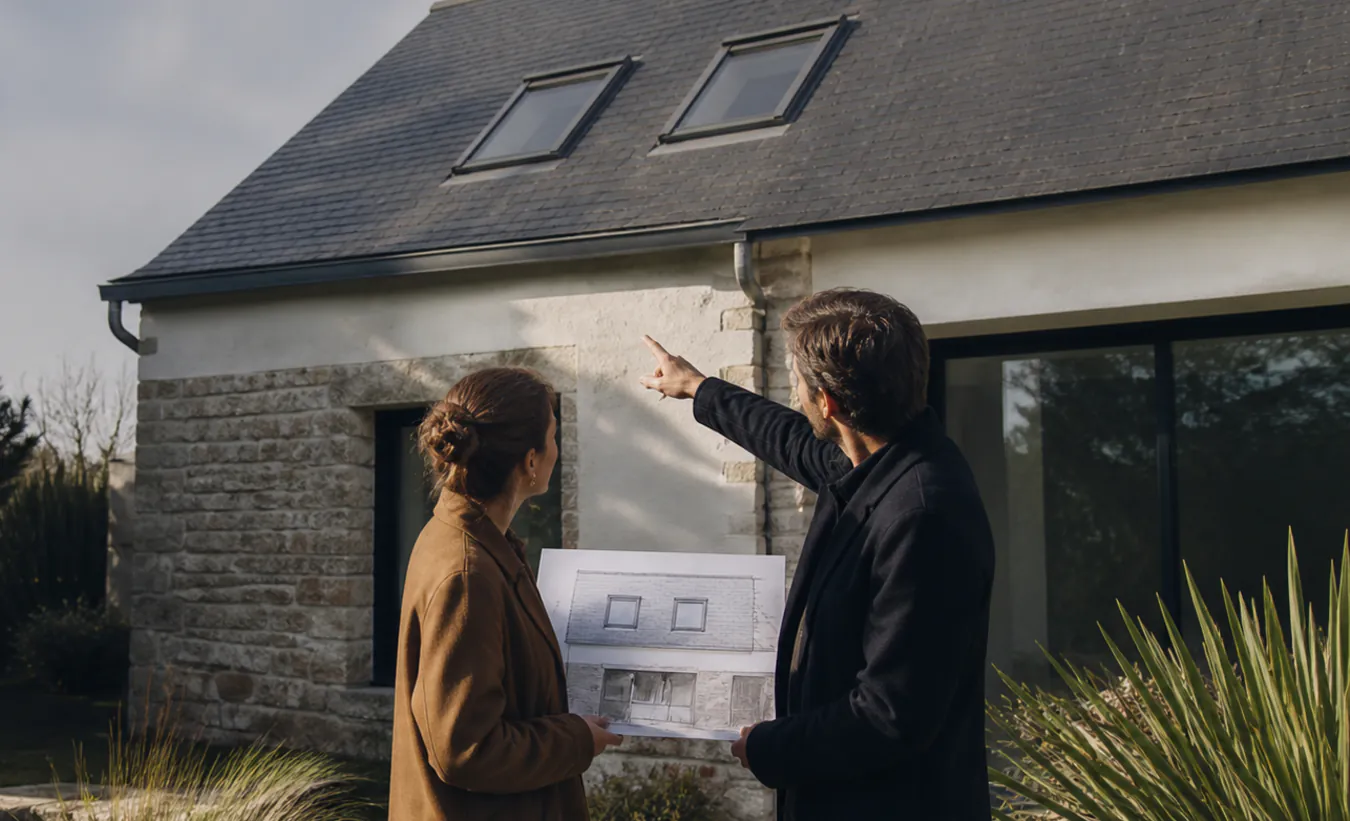 Un architecte et un propriétaire étudient deux fenêtres de toit sur une maison de l'ouest en pierre et ardoise