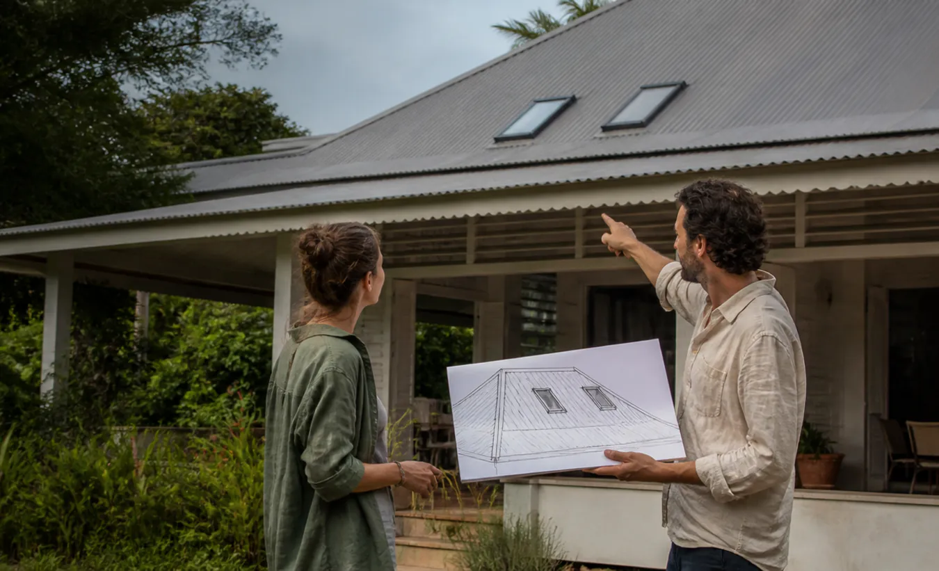 Un architecte et un propriétaire étudient deux fenêtres de toit sur une maison guyanaise à large véranda